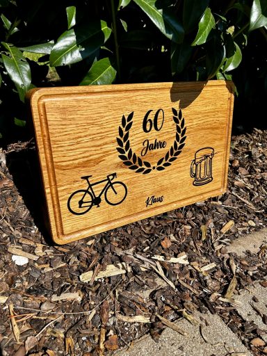 Holzplatte mit Gravur: 60 Jahre, Fahrrad-Symbol und ein weiteres ikonisches Bild.