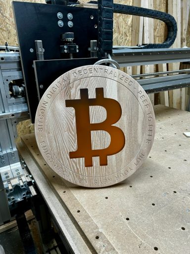 Holzscheibe mit Bitcoin-Logo, auf einem Tisch in einer Werkstatt platziert.